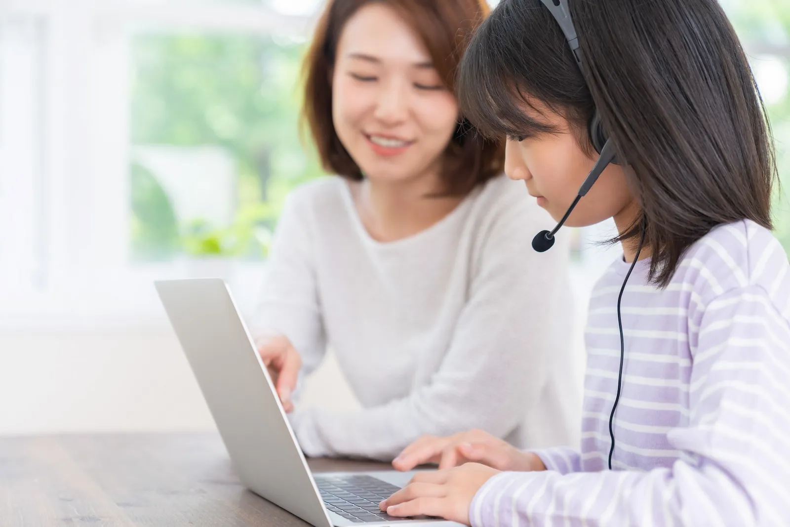 保護者に見守られながらパソコンでオンライン学習に取り組む小学生